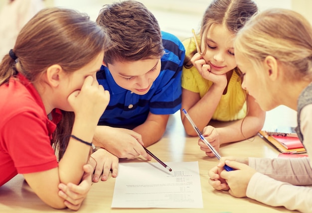 bildung, grundschule, lernen und personenkonzept - gruppe von schulkindern mit stiften und papieren, die im klassenzimmer schreiben