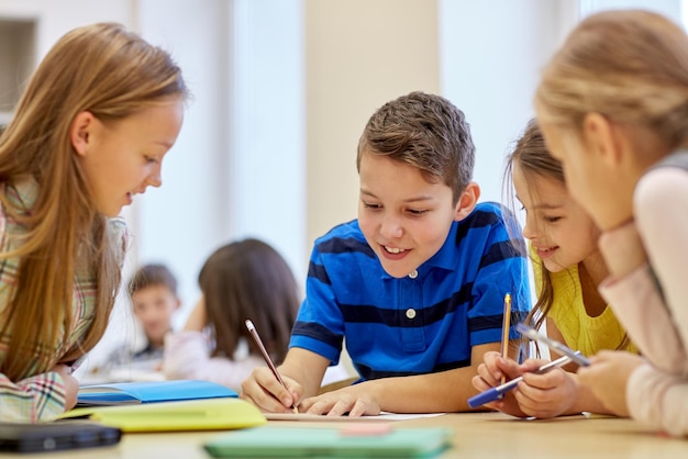 Bildung, grundschule, lernen und personenkonzept - gruppe von schulkindern mit stiften und papieren, die im klassenzimmer schreiben