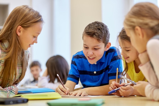 bildung, grundschule, lernen und personenkonzept - gruppe von schulkindern mit stiften und papieren, die im klassenzimmer schreiben