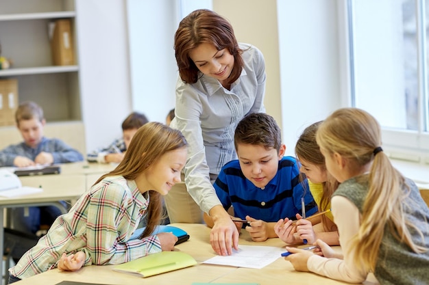 Foto bildung, grundschule, lernen und personenkonzept - lehrer helfen schulkindern beim schreiben von tests im klassenzimmer