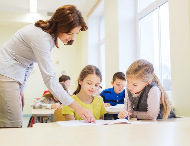 bildung, grundschule, lernen und personenkonzept - lehrer helfen schulkindern im klassenzimmer