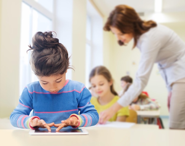 bildung, grundschule, technologie und kinderkonzept - kleines studentenmädchen mit tablet-pc über klassenzimmer- und lehrerhintergrund