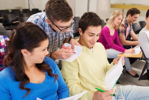 Bildung, Gymnasium, Teamarbeit und People-Konzept - Gruppe lächelnder Studenten mit Notizblöcken, die im Hörsaal sitzen