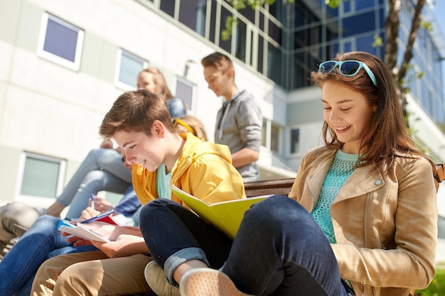 Bildung, High School und People-Konzept - Gruppe glücklicher Teenager mit Notebooks, die auf dem Campus-Hof lernen