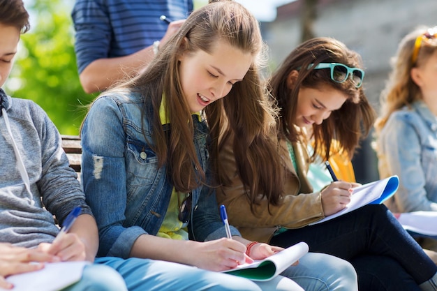 Foto bildung, high school und people-konzept - gruppe glücklicher teenager mit notebooks, die auf dem campus-hof lernen