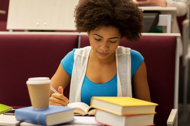 bildung, highschool, universität, lern- und menschenkonzept - afrikanisches studentenmädchen mit büchern und kaffee im vortrag