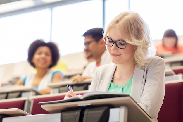 bildung, highschool, universität, lernen und personenkonzept - studentin schreibt im hörsaal an notizbuch