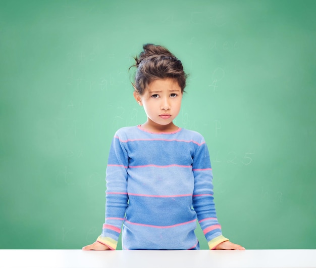Bildung, Menschen, Kindheit und Emotionen Konzept - trauriges kleines Schulmädchen über grünem Kreidetafelhintergrund