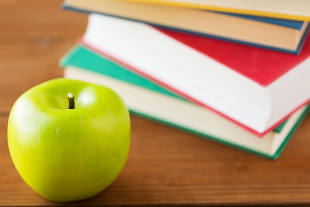 Bildung, Schule, Literatur, Lesen und Wissenskonzept - Nahaufnahme von Büchern und grünem Apfel auf Holztisch