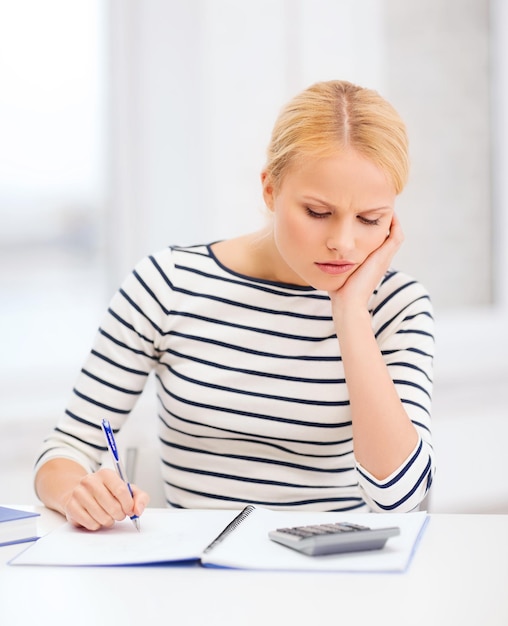 Bildung, Schule und Geschäftskonzept - besorgte Frau mit Notebook und Taschenrechner, die im College studiert