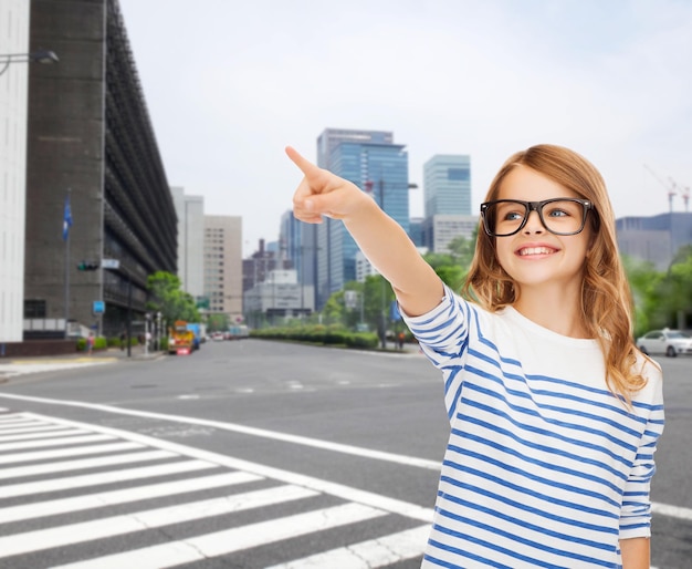 Bildung, Schule und imaginäres Bildschirmkonzept - süßes kleines Mädchen mit Brille, das in die Luft oder imaginären Bildschirm zeigt