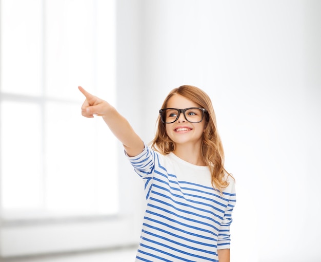 Bildung, Schule und imaginäres Bildschirmkonzept - süßes kleines Mädchen mit Brille, das in die Luft oder imaginären Bildschirm zeigt