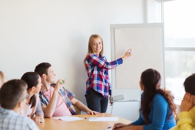 Foto bildung, teamarbeit und personenkonzept - lächelnde studenten mit weißer tafel, die drinnen an einem tisch sitzen