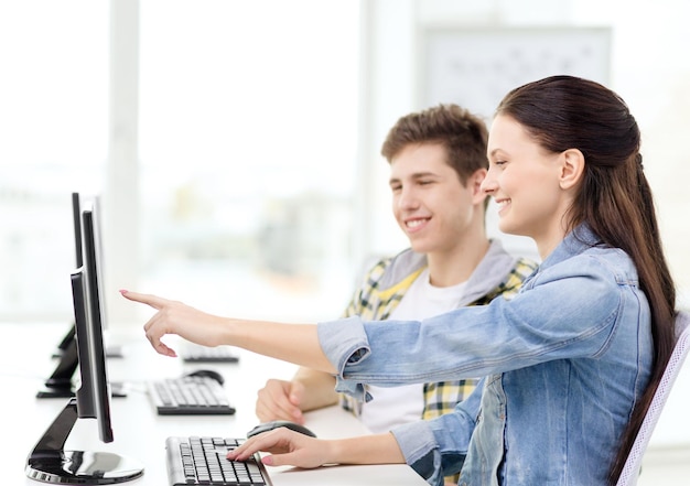 Bildung, Technologie und Schulkonzept - zwei lächelnde Schüler im Computerunterricht, Mädchen, die mit dem Finger auf den Bildschirm zeigen