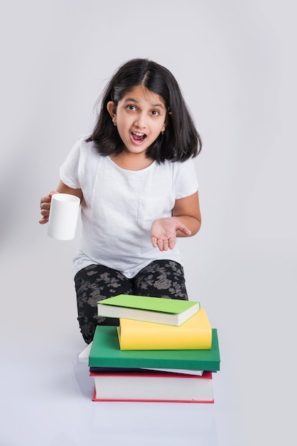 Bildung zu Hause Konzept - Nettes kleines indisches oder asiatisches Mädchen, das mit einem Haufen Bücher und Kaffeebecher studiert, während es zu Hause auf dem Boden sitzt. Auf weißem Hintergrund isoliert