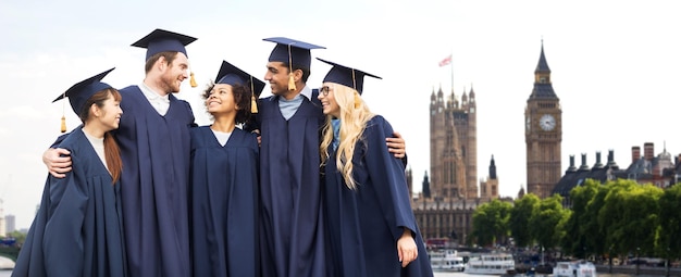 Bildungs-, Abschluss- und Personenkonzept - Gruppe glücklicher internationaler Studenten in Mörtelbrettern und Junggesellenroben vor dem Hintergrund der Londoner Stadt