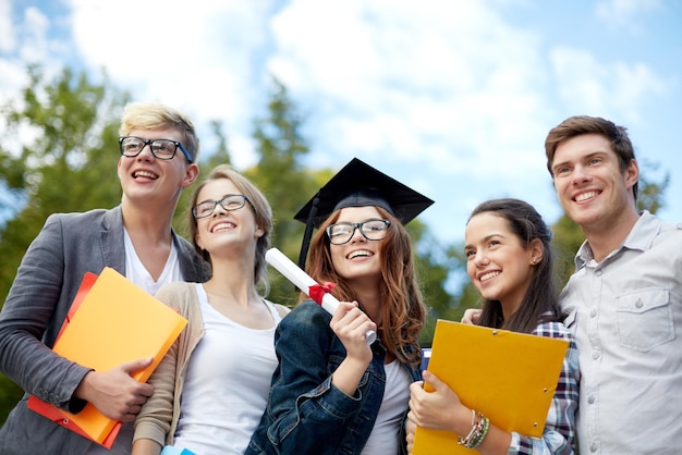 Bildungs-, Abschluss- und Personenkonzept - Gruppe lächelnder Studenten in Doktorhut mit Diplom- und Schulordnern