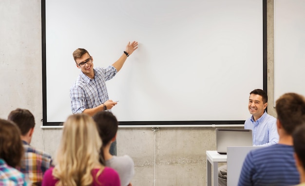 Foto bildungs-, highschool-, technologie- und menschenkonzept - schüler, der mit fernbedienung, laptop-computer vor lehrer und klassenkameraden im klassenzimmer steht