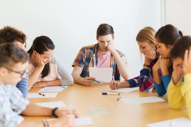 bildungs-, schul-, test- und menschenkonzept - gruppe von studenten mit papieren, die denken oder test machen