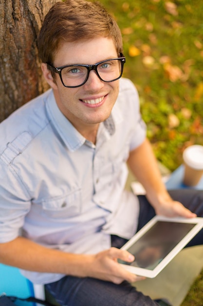 Foto bildungs-, technologie- und internetkonzept - lächelnder männlicher student in brillen mit tablet-pc draußen