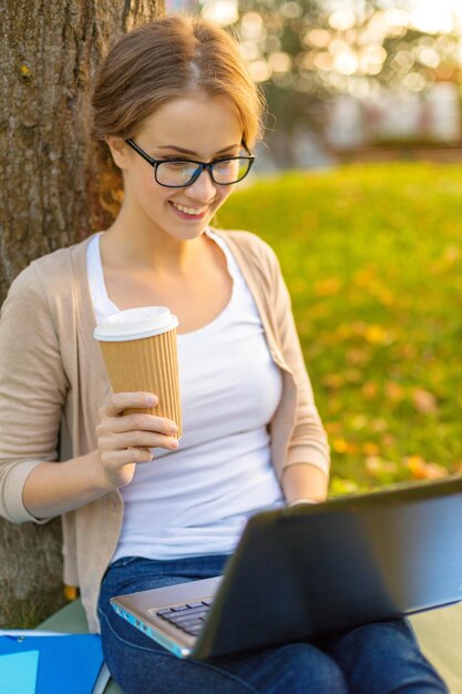 Bildungs-, Technologie- und Internetkonzept - lächelnder Teenager in Brille mit Laptop-Computer und Kaffee oder Tee zum Mitnehmen