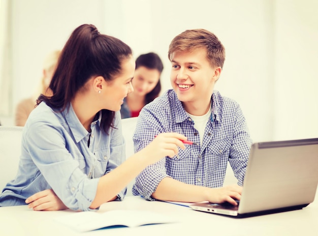 bildungs-, technologie- und internetkonzept - zwei lächelnde schüler mit laptop-computer und notizbüchern in der schule