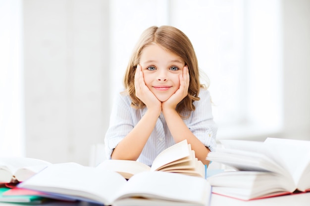 Bildungs- und Schulkonzept - kleine Schülerin, die in der Schule Bücher studiert und liest