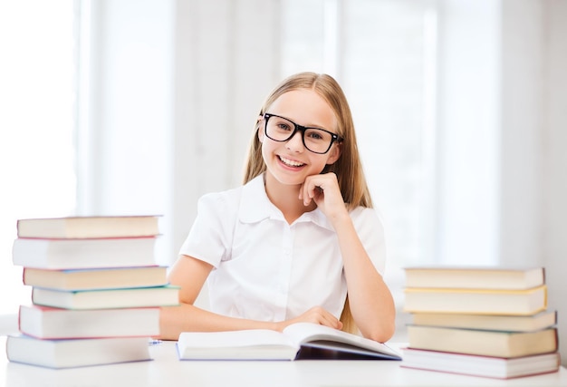 Bildungs- und Schulkonzept - kleine Schülerin, die in der Schule Bücher studiert und liest