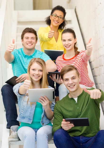 bildungs- und technologiekonzept - lächelnde studenten mit tablet-pc-computer, die auf der treppe sitzen und daumen hoch zeigen