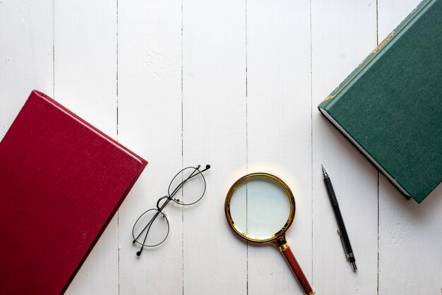 Bildungsbuchkonzept Stift Brille Lupe auf weißem Holzhintergrund