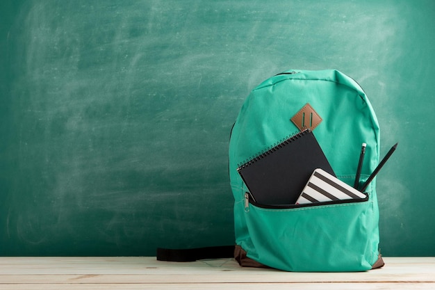 Foto bildungskonzept - blauer rucksack, schwarze notizbücher und bleistifte auf dem hintergrund der tafel