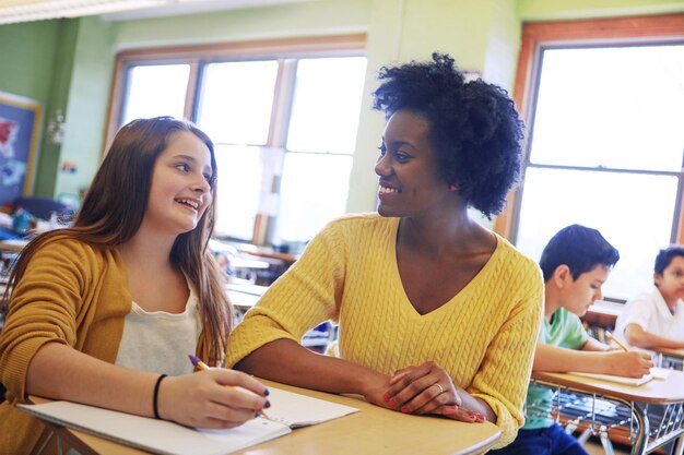 Bildungslernen und Lehrer helfen Schülern bei Aufgaben in der Grundschule Klassenunterstützungsstipendium und glückliche schwarze Frau oder Erzieherhilfe, die Lernenden im Unterricht erklärt und hilft