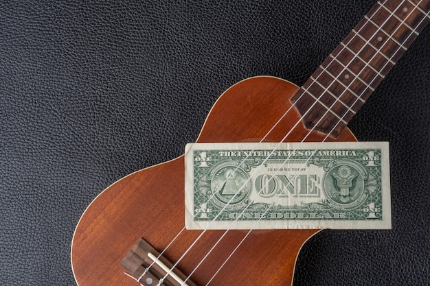 Un billete de un dólar está en un ukelele con un ukelele a un lado.