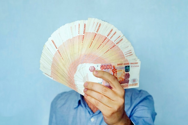 Billetes de banco rusos rublos en mano. 5000 billetes de banco plegados en abanico cubren el rostro del empresario.