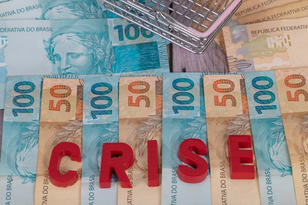 Billetes brasileños Billetes de 50 y 100 reales en el fondo con la palabra crisis en portugués crisis en inglés en rojo Enfoque selectivo