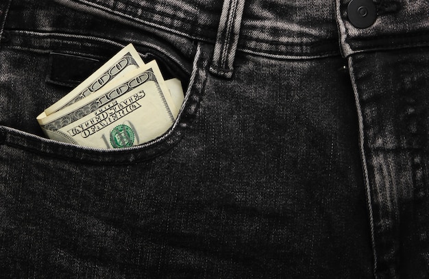 Billetes de cien dólares en el bolsillo delantero del primer plano de jeans negros.