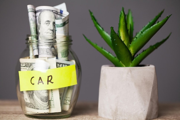 Billetes de dólar en tarro de cristal y coche de texto en mesa de madera