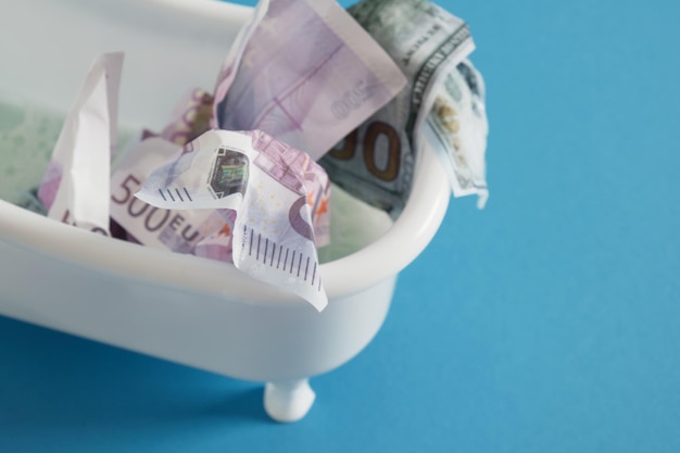 Billetes de euro y dólar en una tina pequeña sobre una espuma de fondo nevada sobre el lavado de dinero