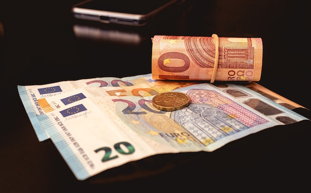Billetes en euros y una sola moneda en un escritorio de oficina de color oscuro