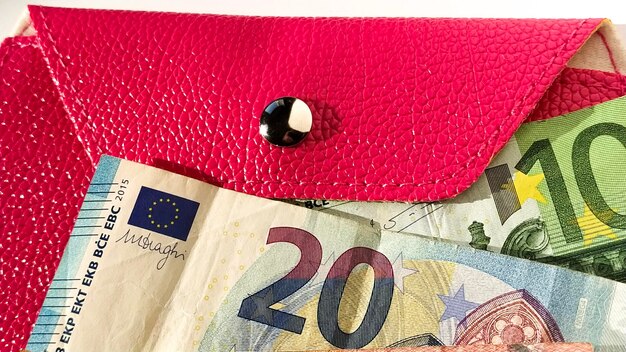 Billetes de papel euro Moneda europea sobre fondo blanco Cartera o monedero en rosa brillante con un botón metálico brillante Billetes del Banco Central por 20 y 100 euros