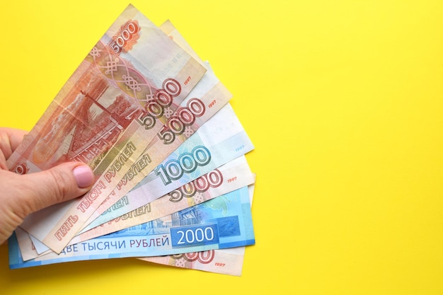 Billetes de rublo ruso en una mano femenina sobre un fondo amarillo Copie el espacio