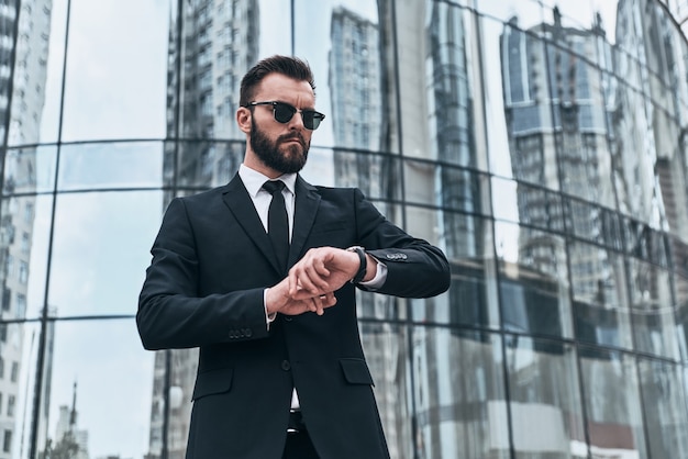 Bin ich spät? Gut aussehender junger Mann in vollem Anzug und Sonnenbrille, der die Zeit überprüft