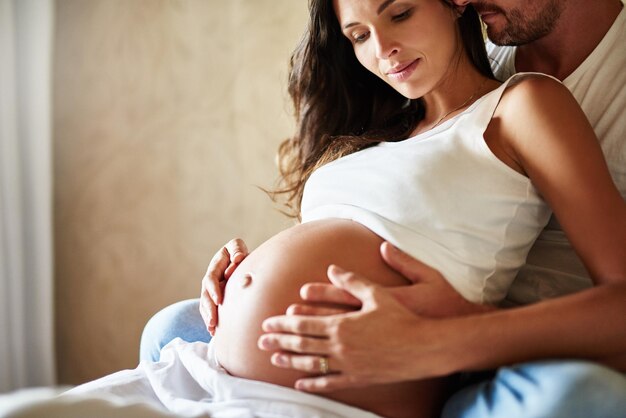 Bindung mit dem Baby Aufnahme eines Mannes und einer schwangeren Frau, die zusammen in einem Schlafzimmer sitzen