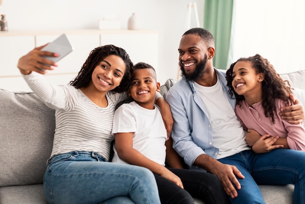 Foto bindung und lebensstil. porträt einer afroamerikanischen familie, die zu hause zusammen selfie macht. glückliche eltern posieren mit ihren kindern und lächeln in die kamera, sitzen auf der couch im wohnzimmer