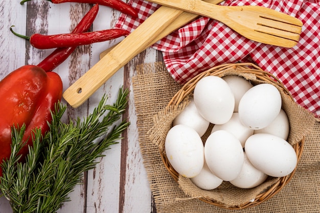 Bio-Bauernhof weiße Eier in einem Korb auf einem rustikalen Holztisch mit Chilischoten und Rosmarin.