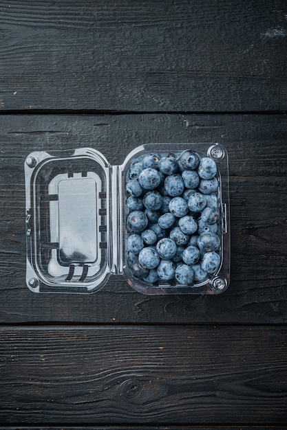 Bio-Blaubeeren in Plastikboxverpackung, auf schwarzem Holztischhintergrund, Draufsicht flach legen