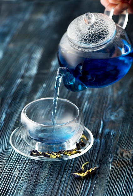 Bio-Blautee Anchan in einer Teekanne und einer Tasse auf blauem Holzhintergrund