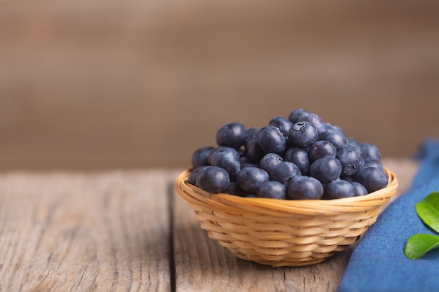 Bio-Heidelbeeren in Korbschale auf Holzuntergrund mit blauer Serviette und Blatt. Selektiver Fokus