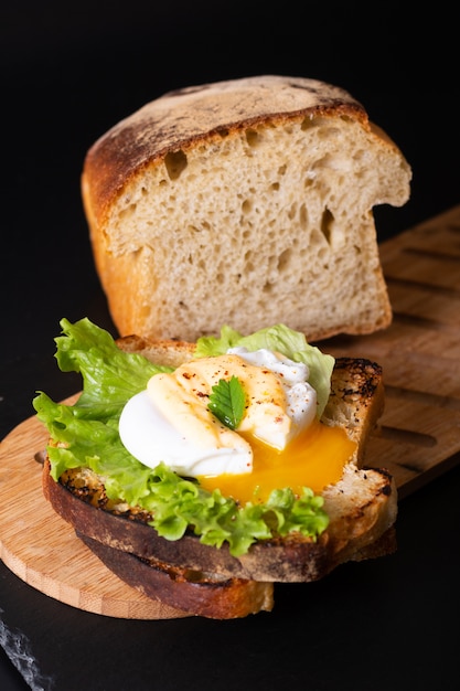 Bio-Lebensmittel-Frühstückskonzept hausgemachtes pochiertes Ei oder Eier Benedict auf Sauerteigbrot geröstet auf schwarzem Schieferbrett