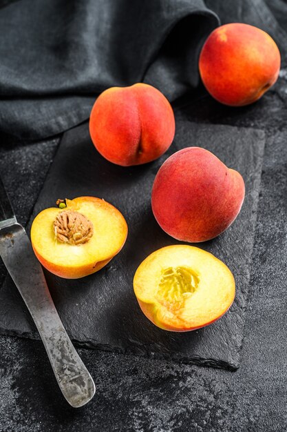 Bio-Pfirsichfrucht auf einem schwarzen Steinbrett. Schwarzer Hintergrund. Draufsicht.